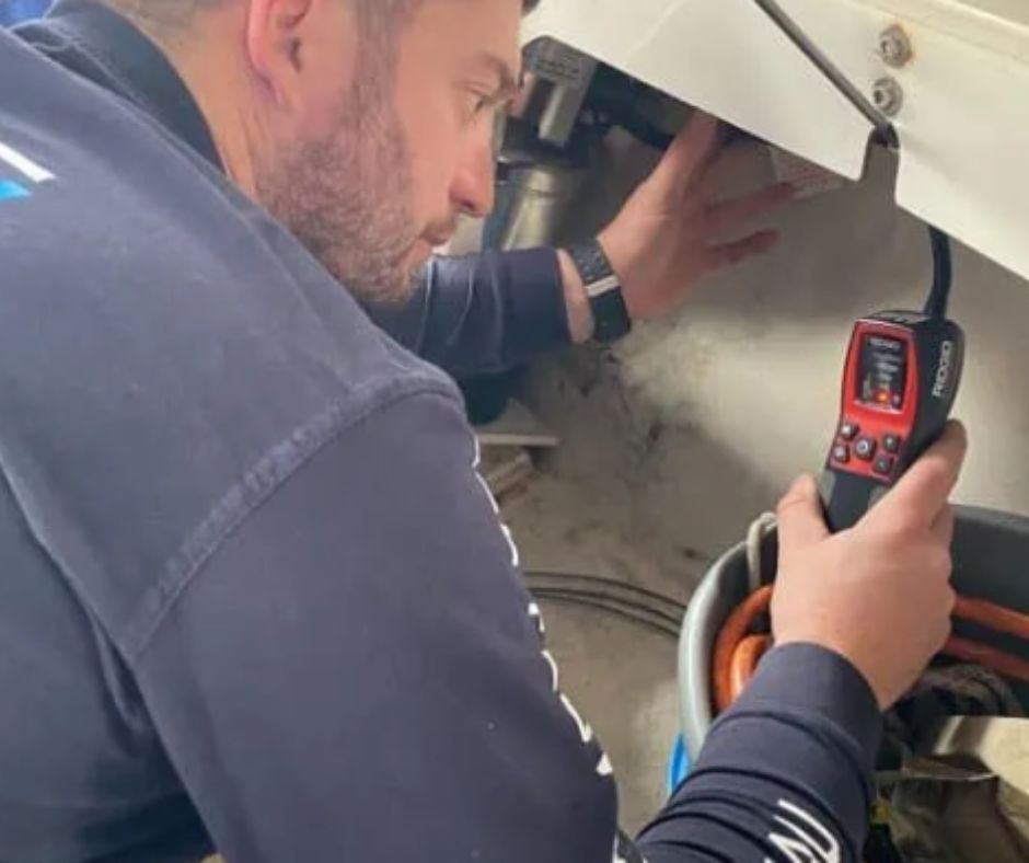 A person uses a handheld diagnostic tool to inspect equipment in a confined space.
