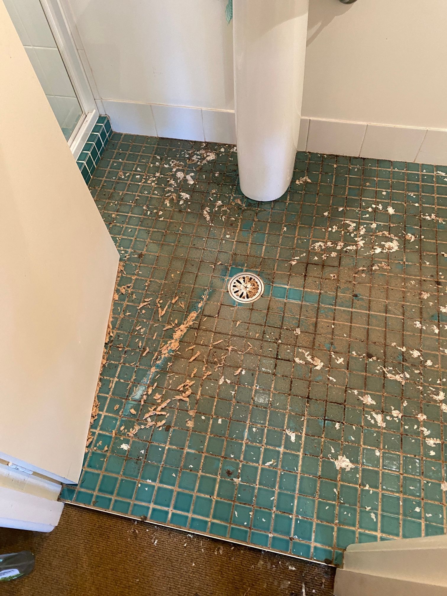 A bathroom floor covered in white paint spatters, showing a drain, tiled flooring, and a sink pedestal.