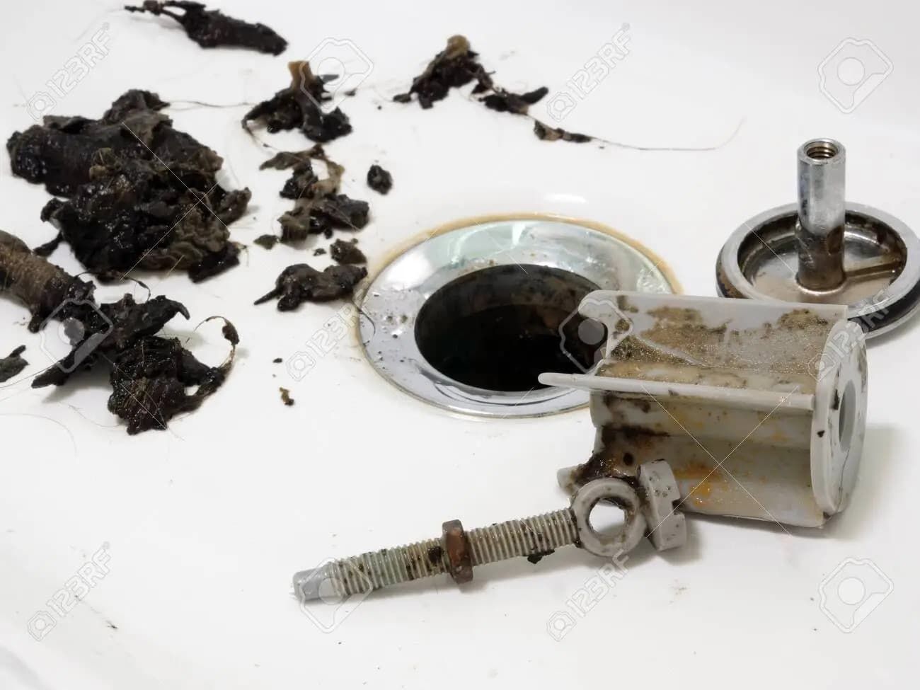 A pile of dark hair and debris removed from a bathtub drain, with the metal drain stopper and hardware lying nearby.
