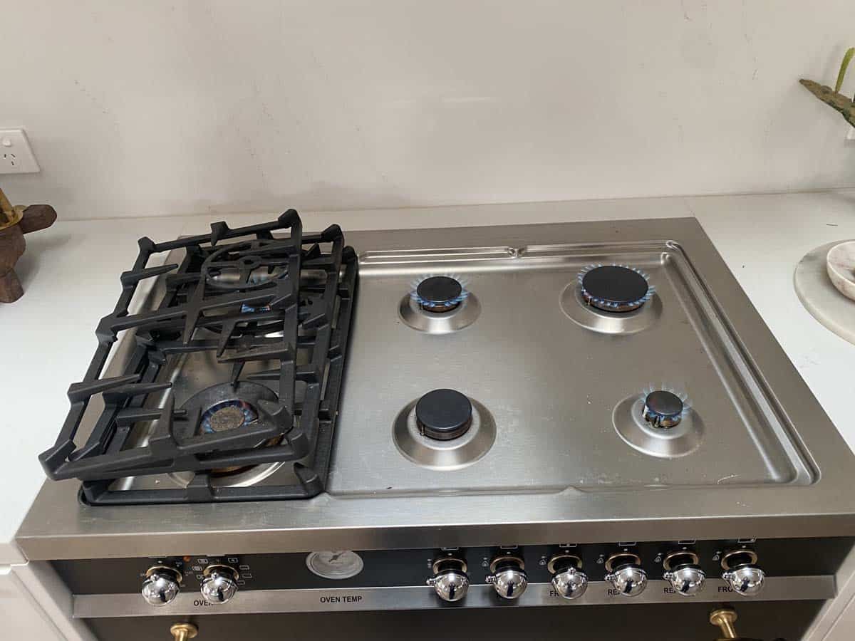 A stainless steel gas stove with a heavy cast-iron grate covering the left burners and four exposed burners on the right.