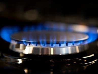 A close-up of a kitchen stove burner ignited with a bright blue flame.