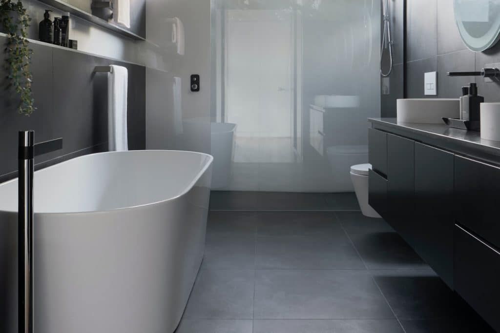 A modern bathroom featuring a white freestanding bathtub, a dark gray vanity, and a large walk-in glass shower.
