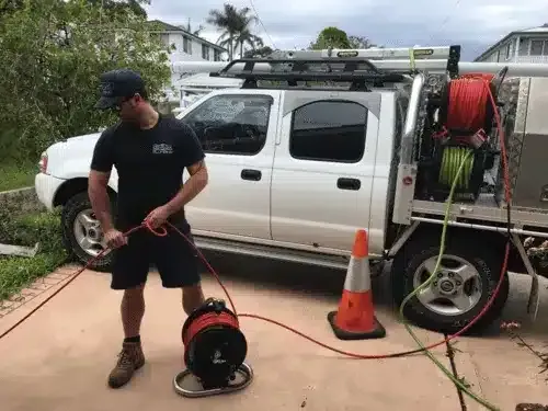 A worker reels a drain inspection camera cable next to a white service truck in a driveway.