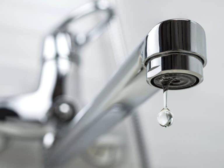 A shiny metal faucet dripping a single clear water droplet against a white background.