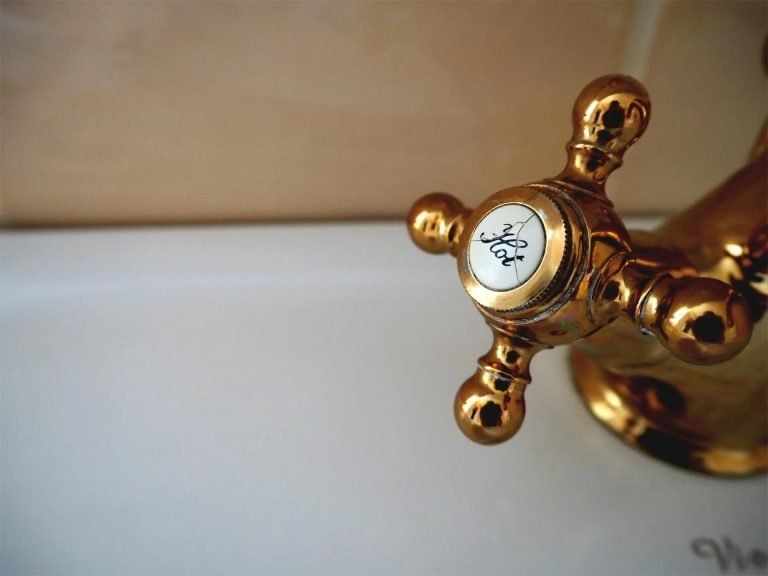 A close-up view of a polished, gold-tone bathroom faucet handle with a small crack in its circular white 