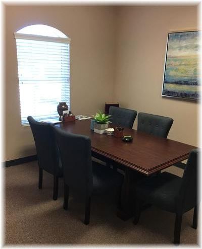 Professional conference room setup with wooden table, upholstered chairs, indoor plant, and window lighting