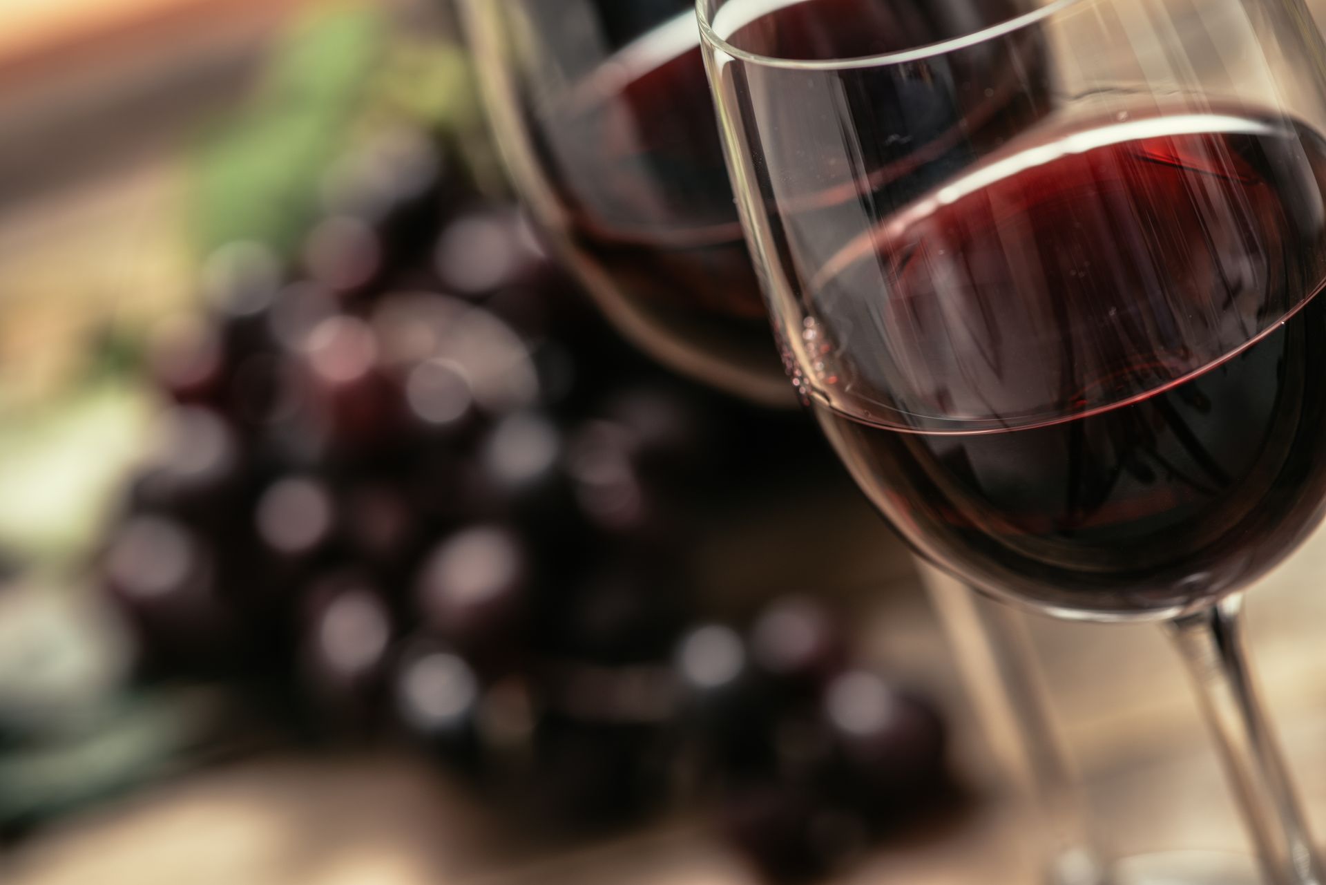 Three glasses of red wine with grapes in the background