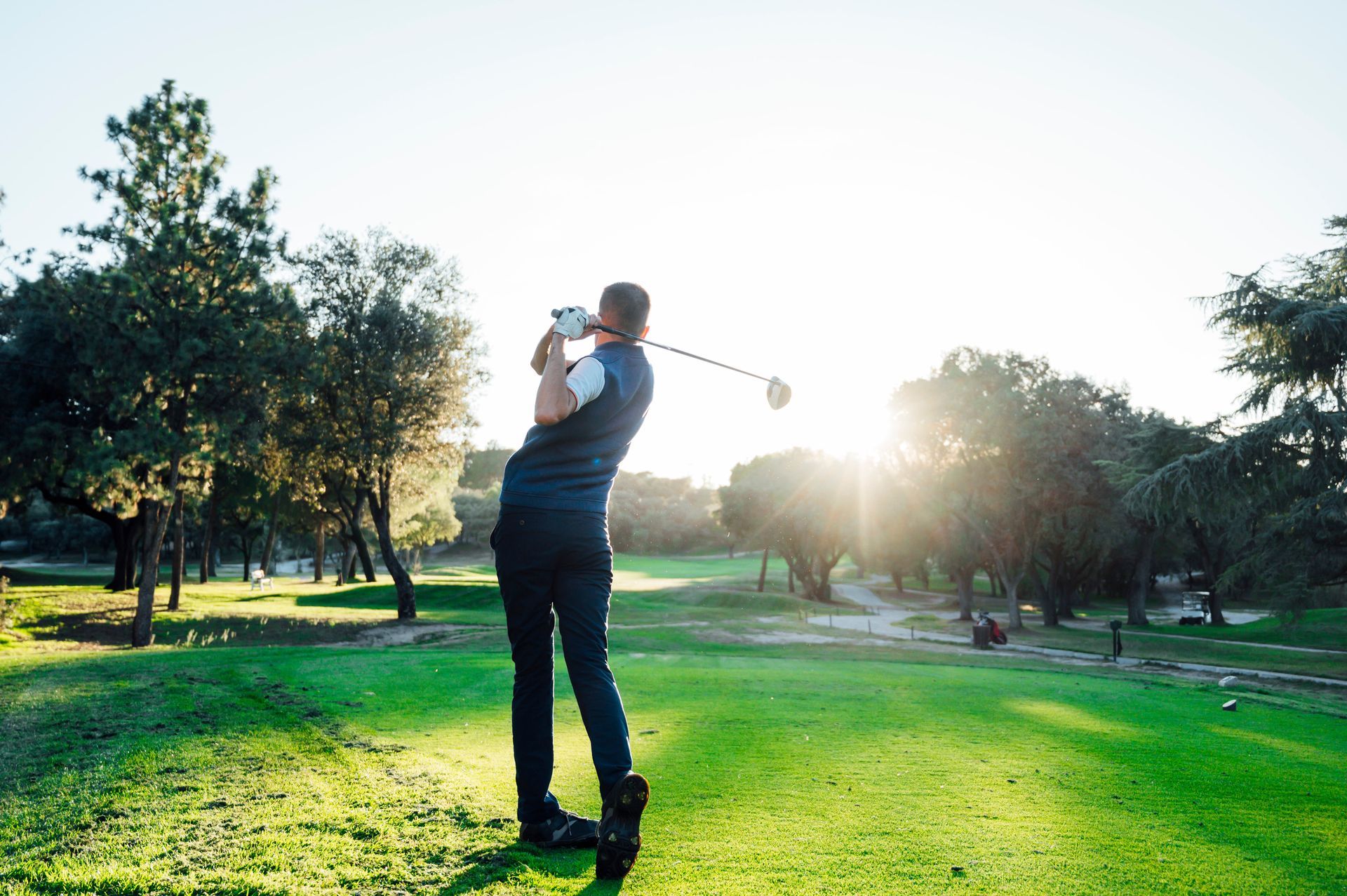 Golfer swinging club on a sunny golf course.
