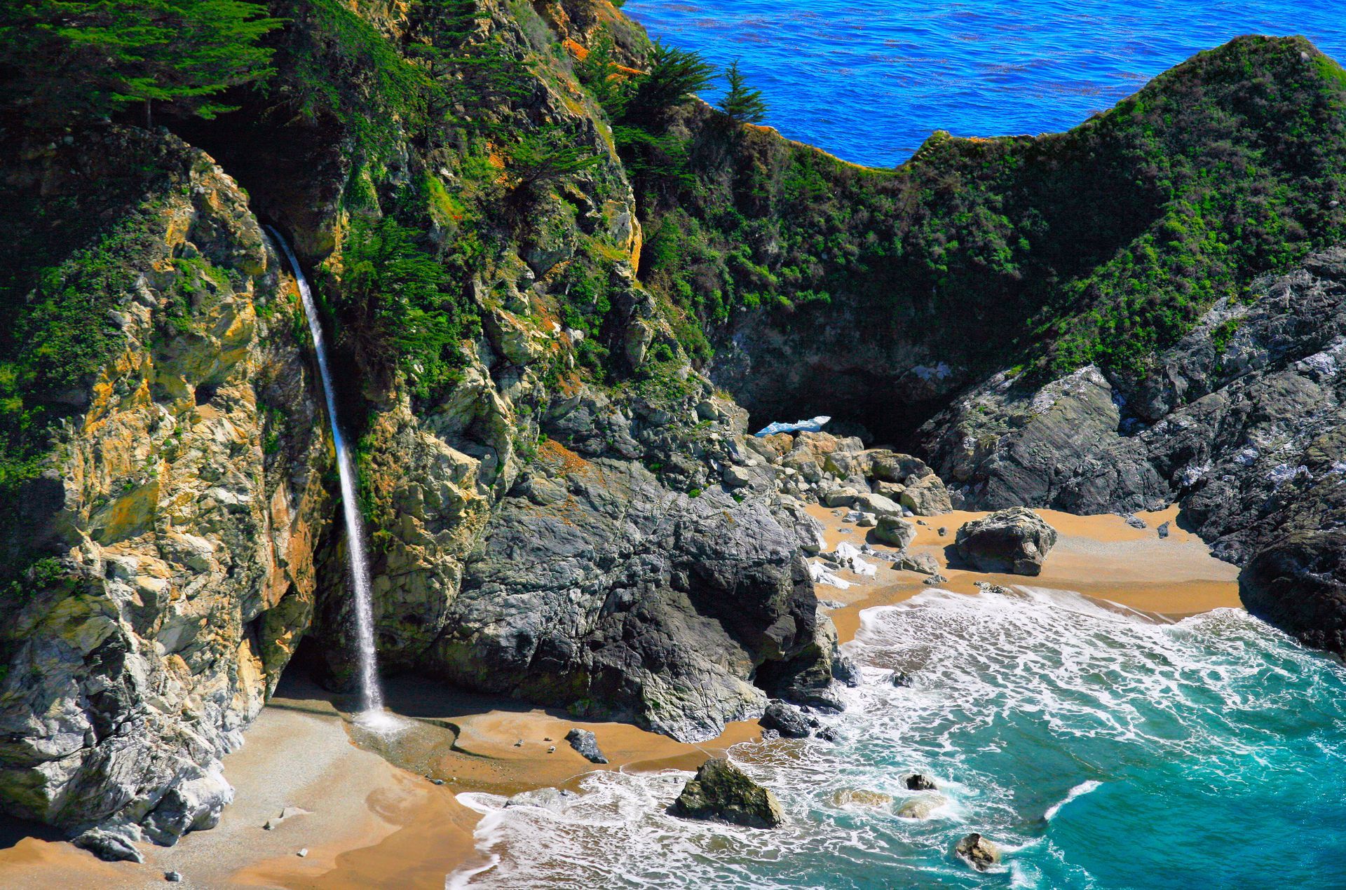 A waterfall is coming down a cliff into the ocean