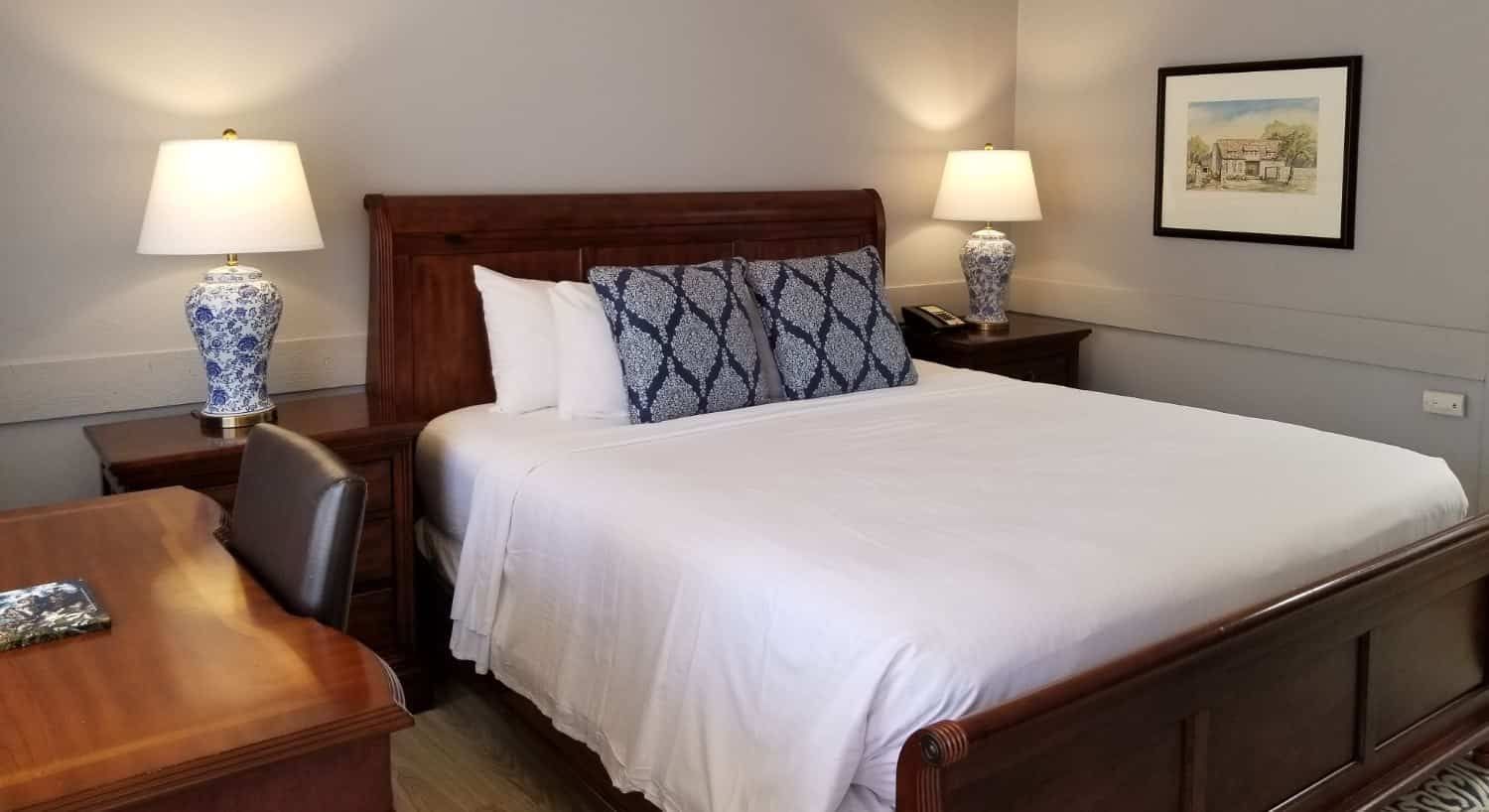 A hotel room with a bed , two lamps , a desk and a chair.