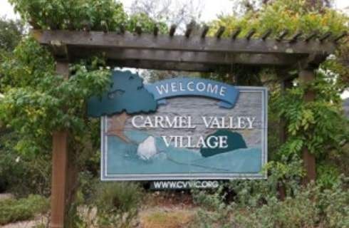 A welcome sign for carmel valley village is surrounded by trees and bushes.