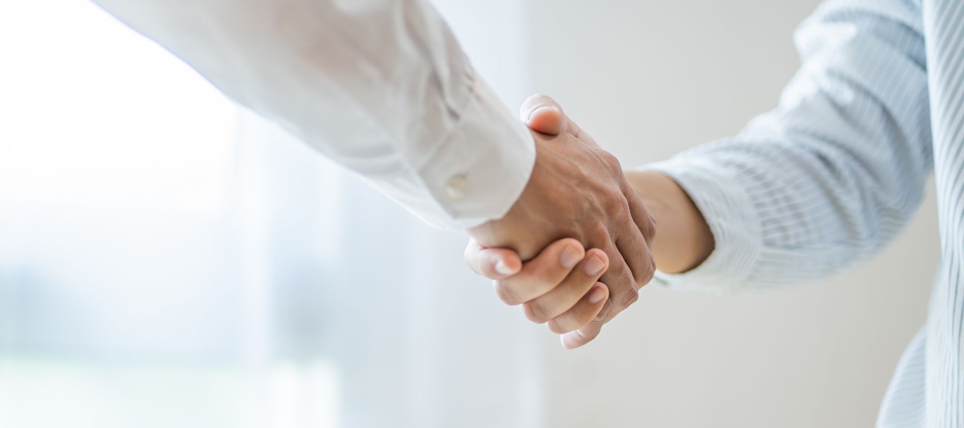 A man and a woman are shaking hands in front of a window.