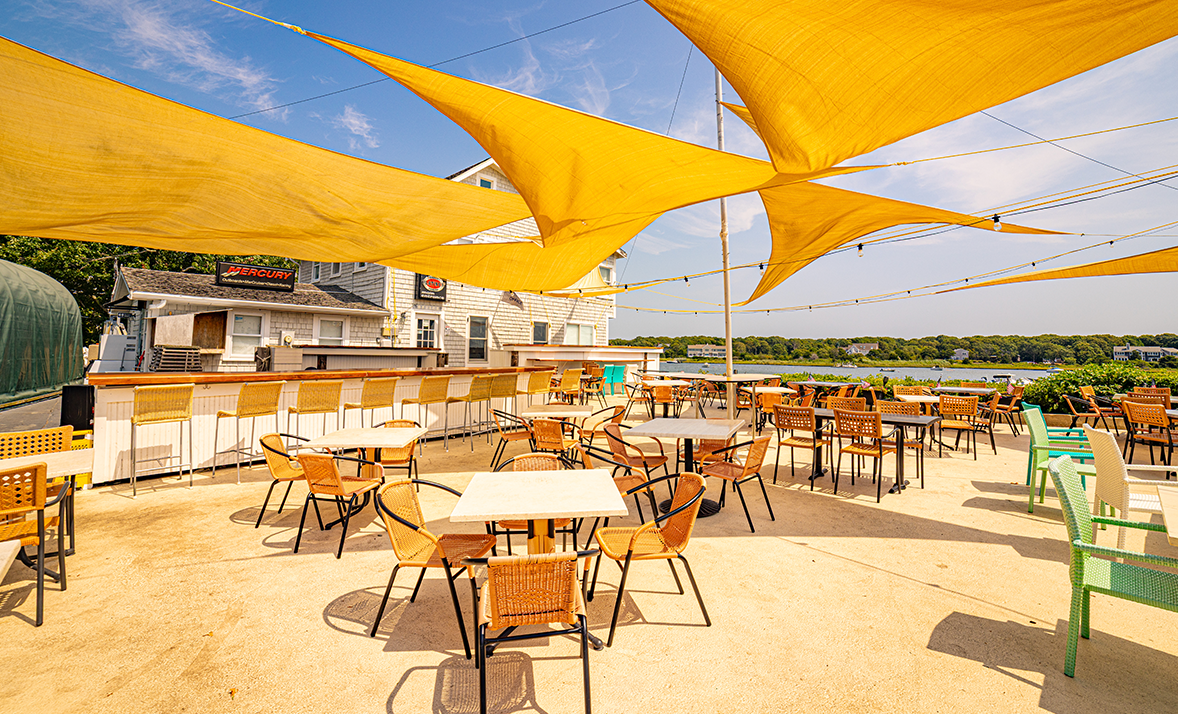 A patio with tables and chairs under umbrellas overlooking a body of water.