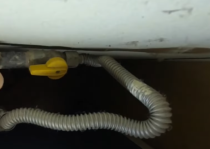 Yellow gas valve connected to a flexible corrugated tube, beneath a white surface.