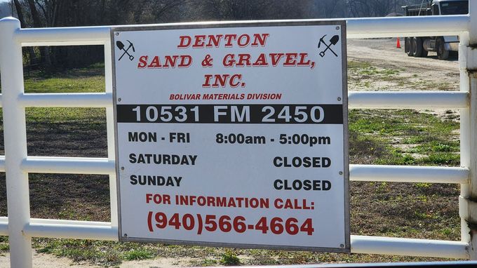 Sign for Denton Sand & Gravel Inc., with address, hours, and phone number on a white metal gate.