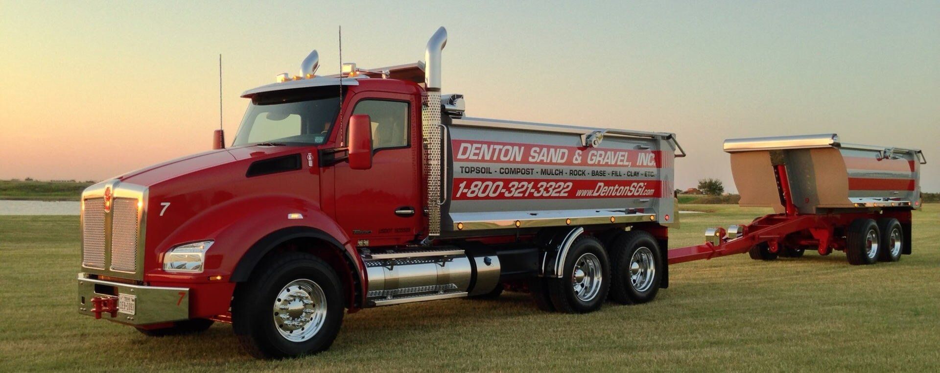 Red semi-truck with trailer, on a grassy field. Truck has company logo