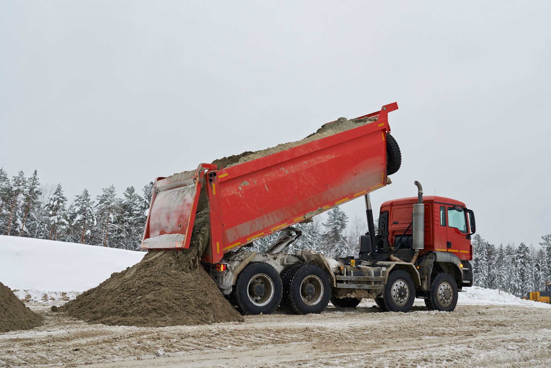 Red dump truck dumping gravel on a snowy construction site. Red dump truck dumping gravel on a snowy construction site.
