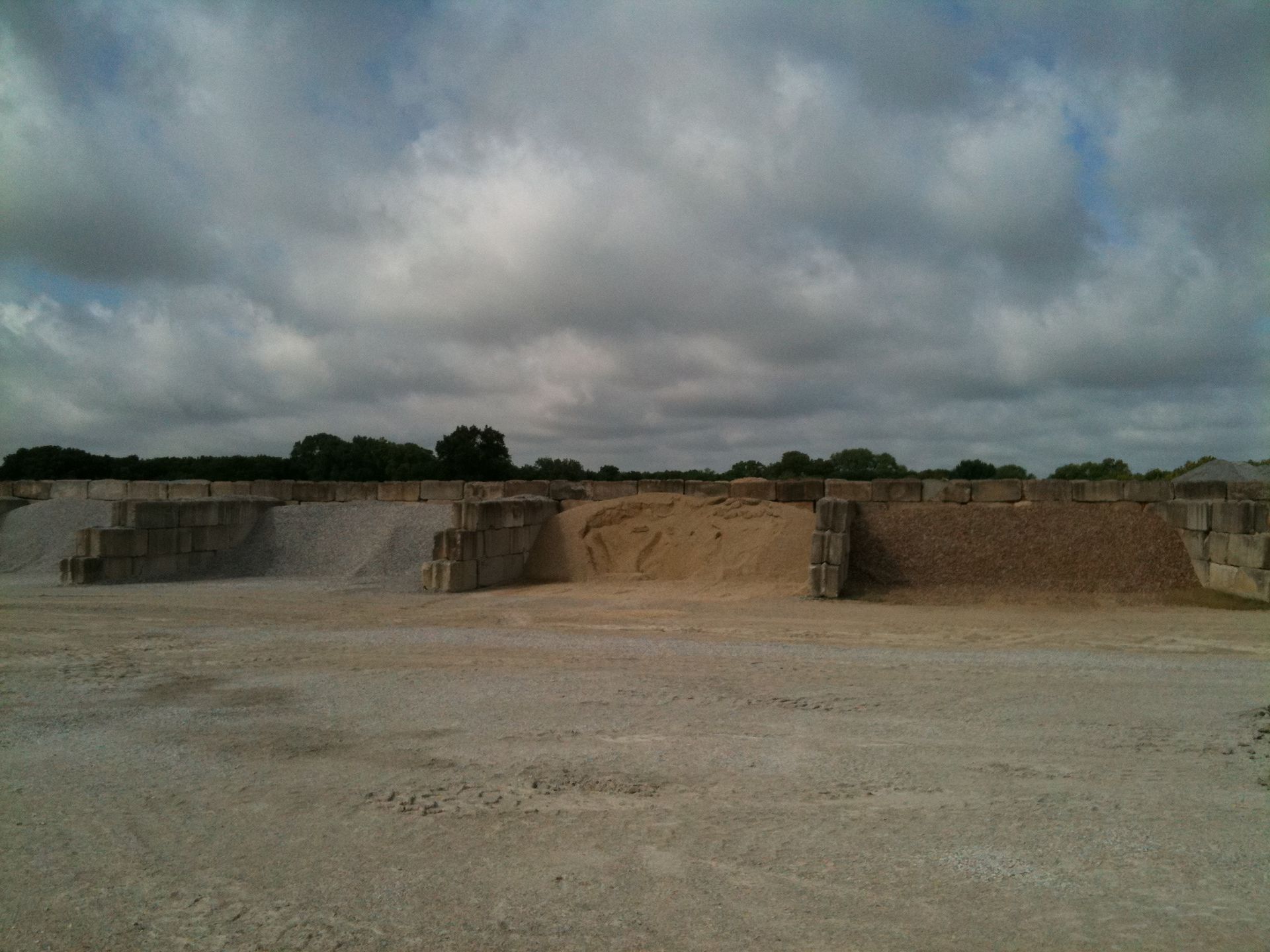 Material yard with piles of different colored gravel under a cloudy sky.