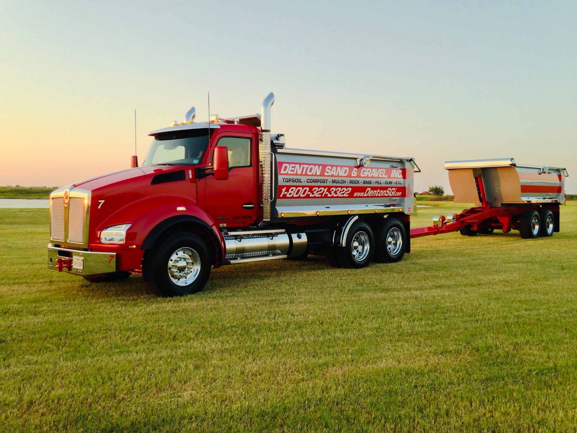 Red dump truck with trailer on green grass, Denton Sand & Gravel Inc.