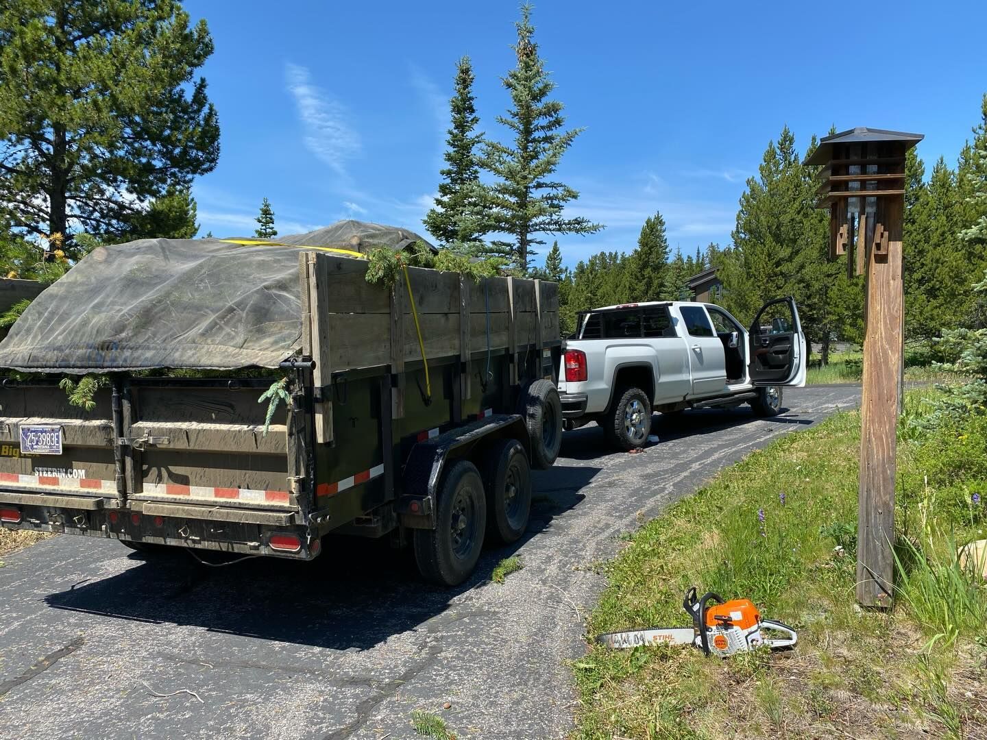 White SUV towing a covered utility trailer on a gravel road, with trees and a birdhouse nearby.