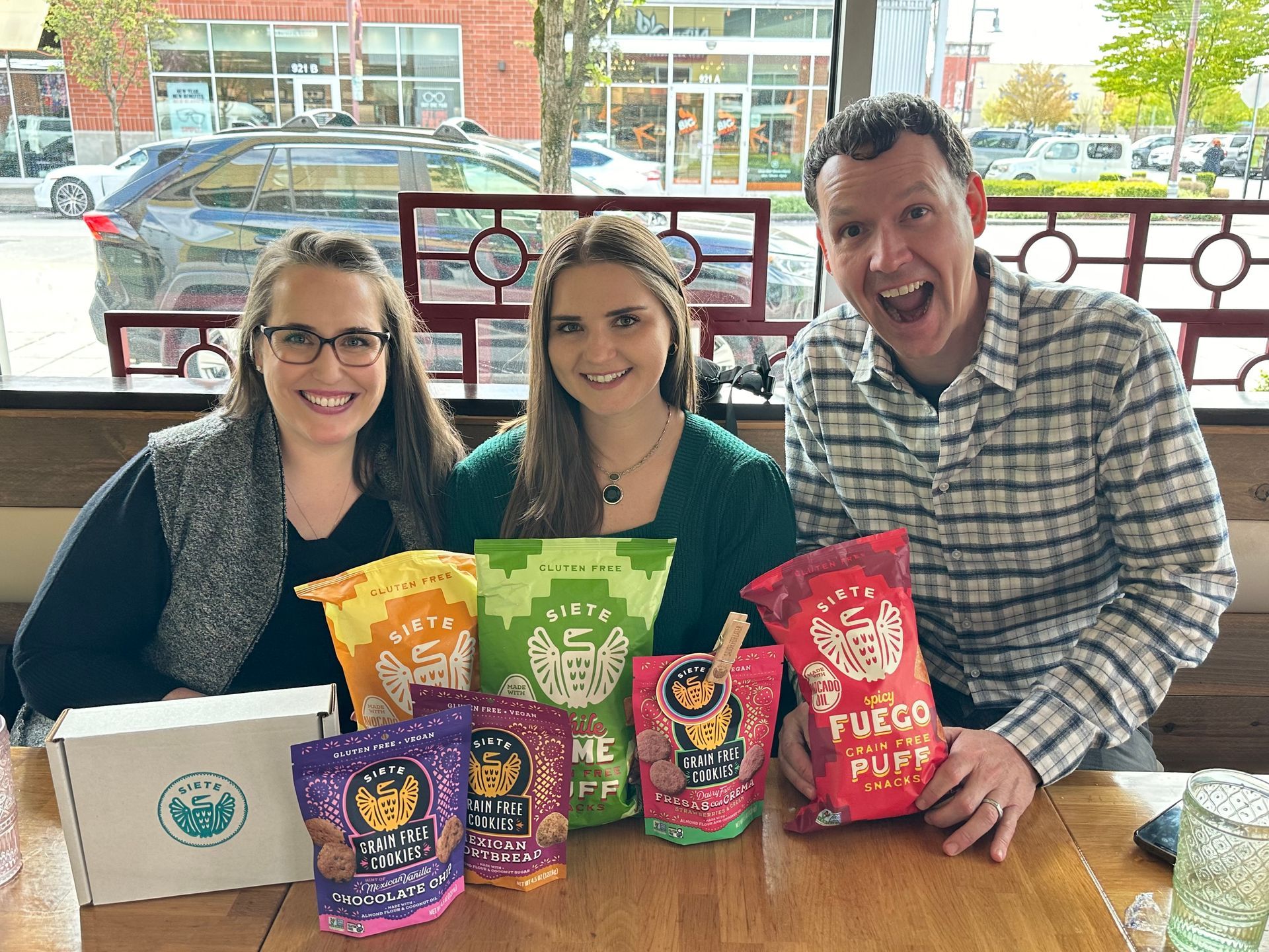 A man and two women are sitting at a table with bags of chips.