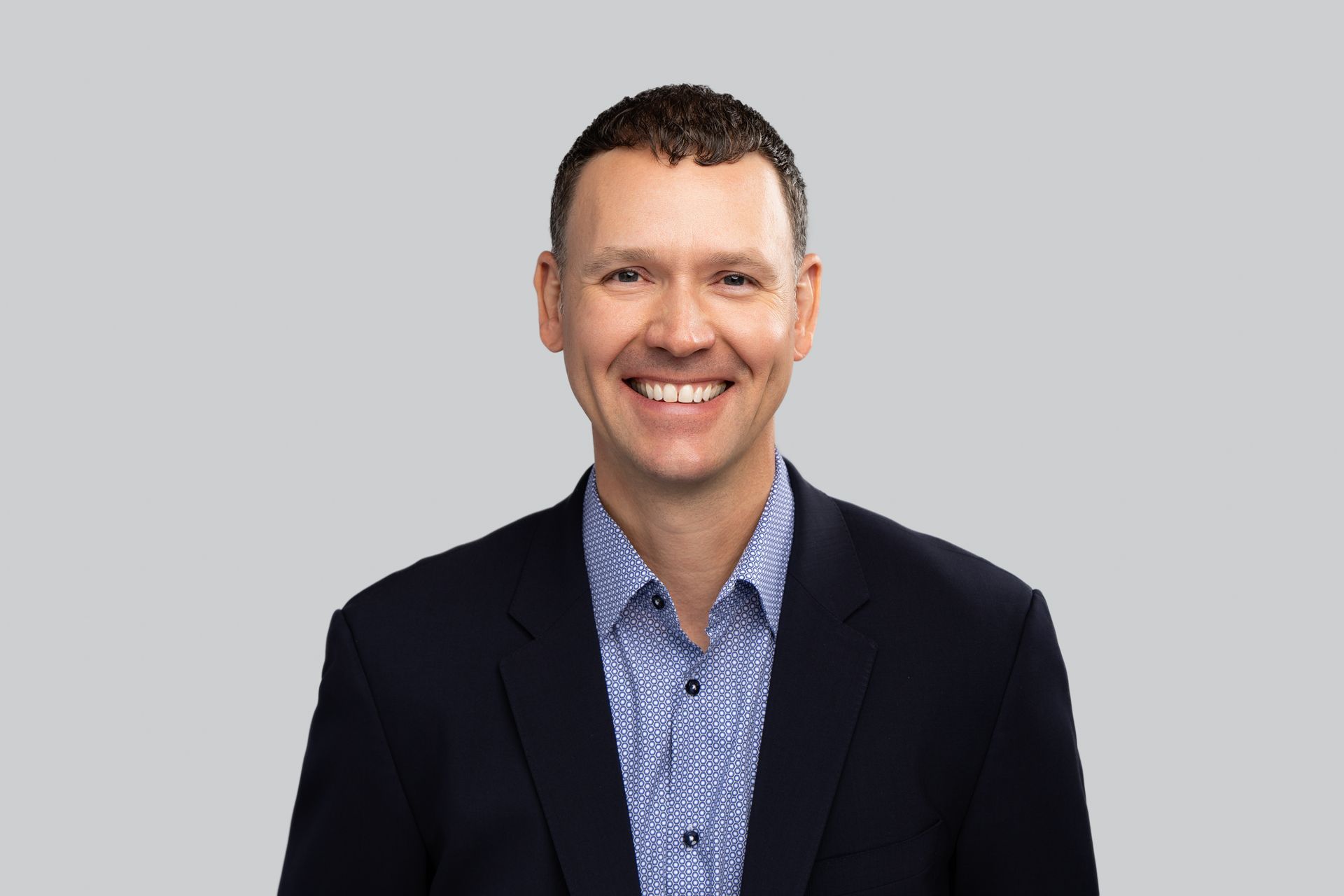 A man in a suit and blue shirt is smiling for the camera.