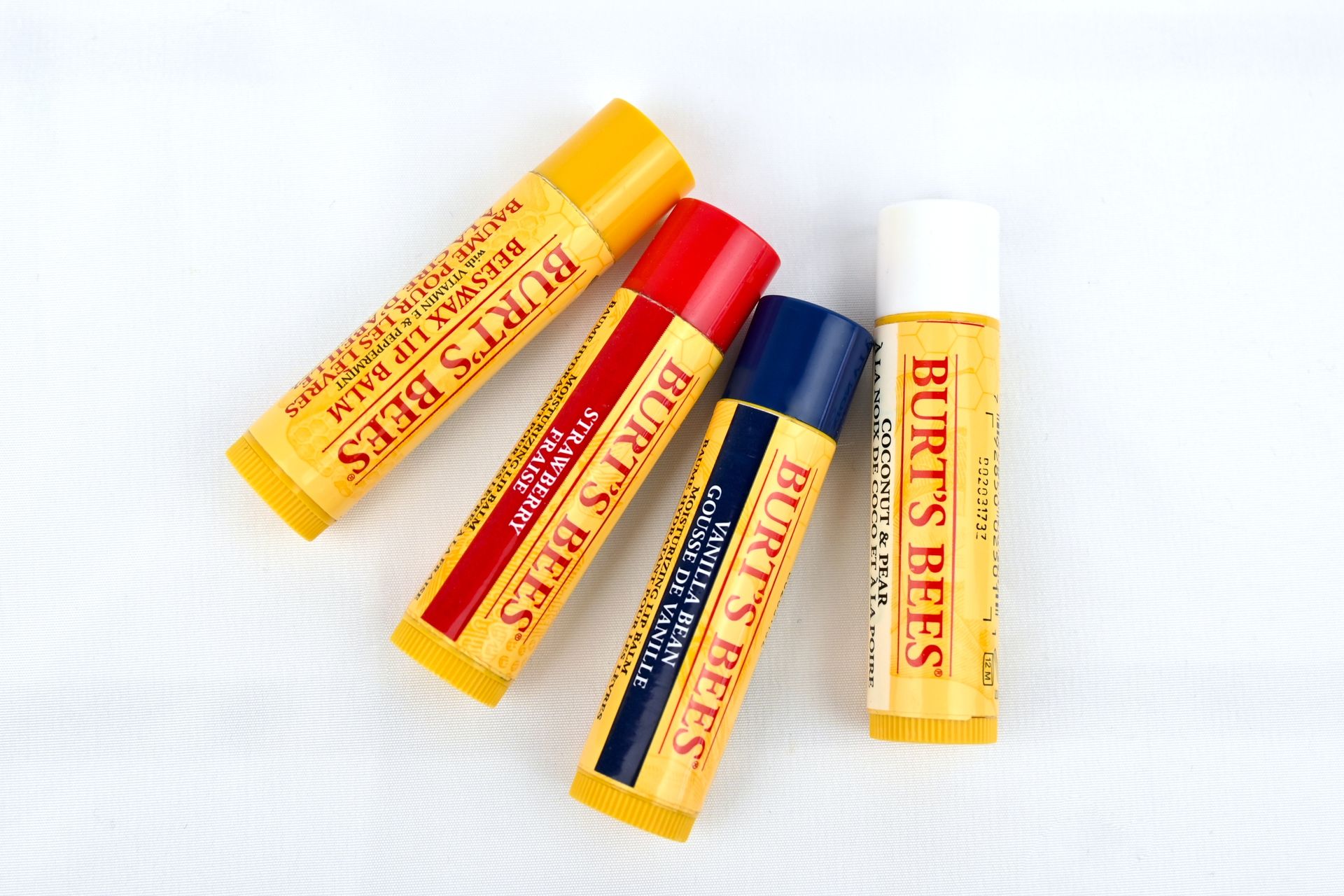 Four burt 's bees lip balms are stacked on top of each other on a white surface.