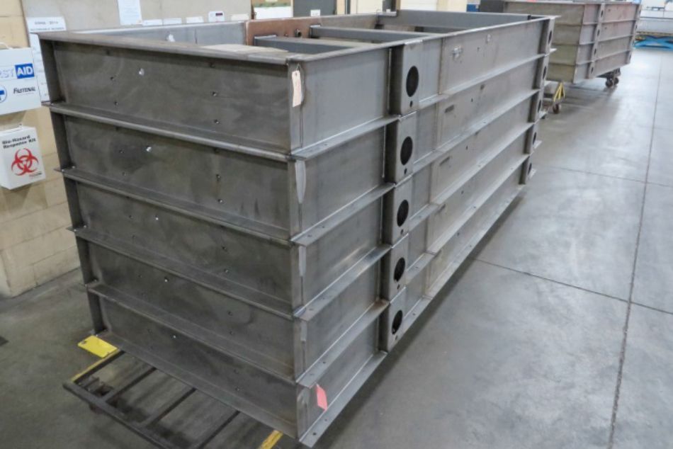 Vertical stack of raw steel structural weldments illustrating a high-capacity production run.