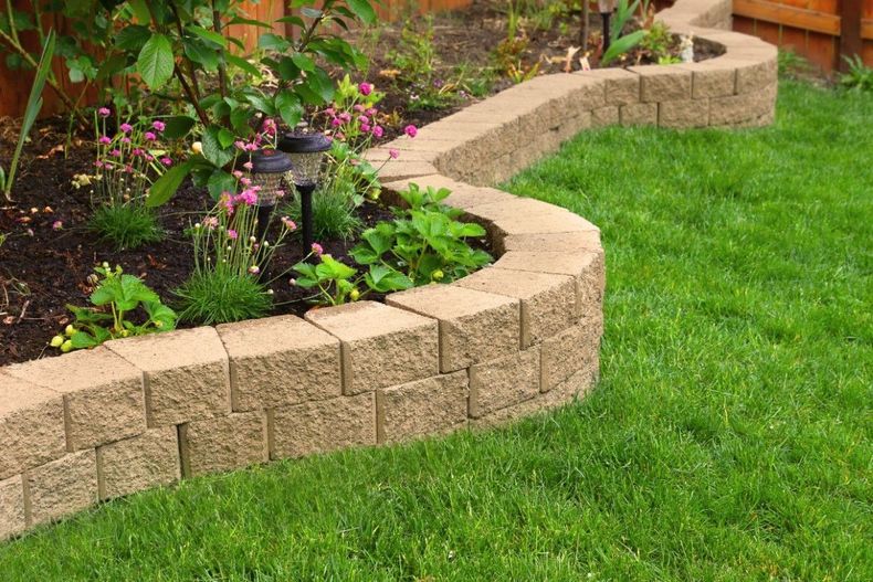 Curved stone garden border edging a lush green lawn with flowering plants