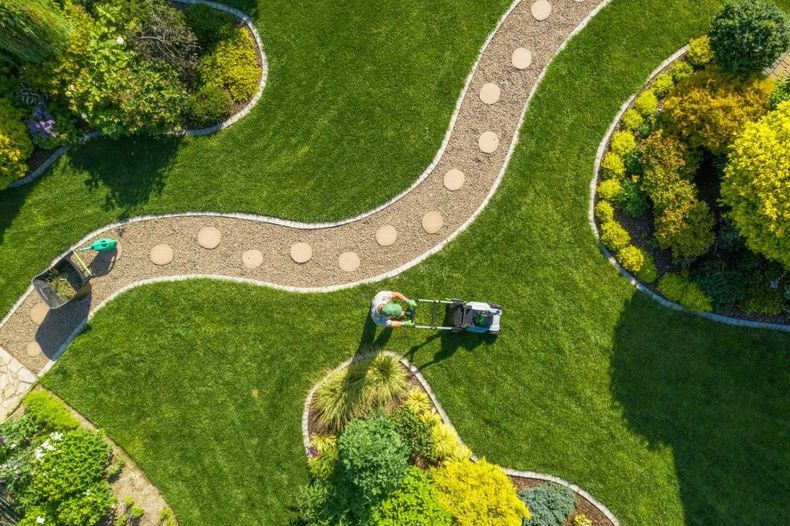 Aerial view of a winding stone path through a green park with benches and trees.