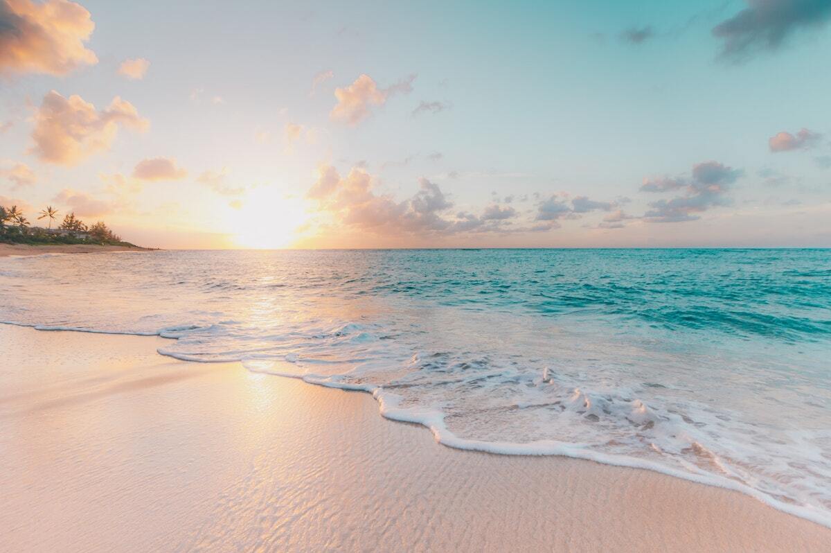 A beach with a sunset in the background and waves crashing on the sand.