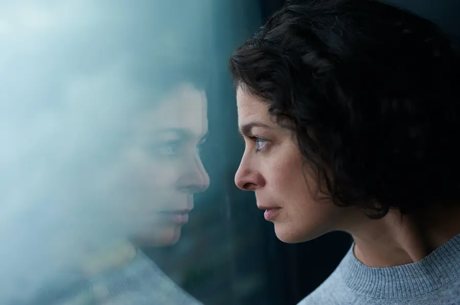 A woman is looking out of a window at her reflection.