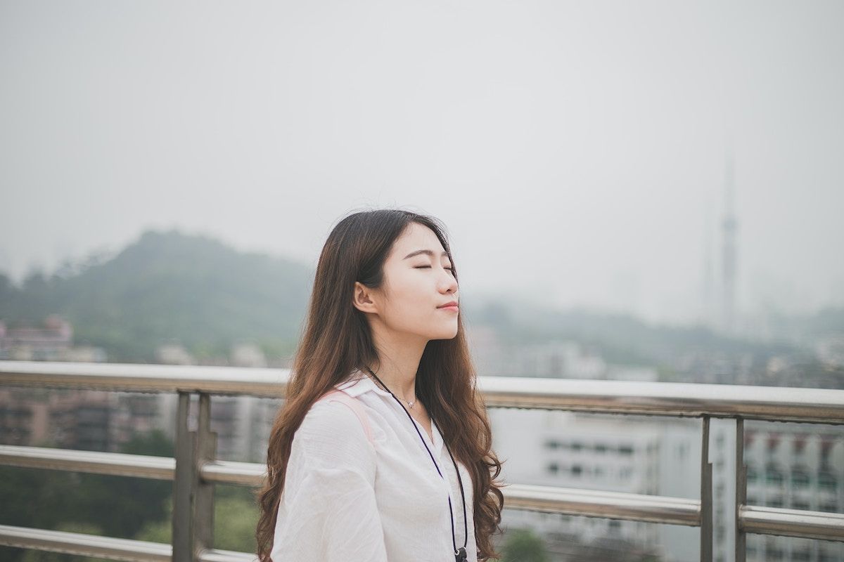 A woman is standing on a balcony with her eyes closed.