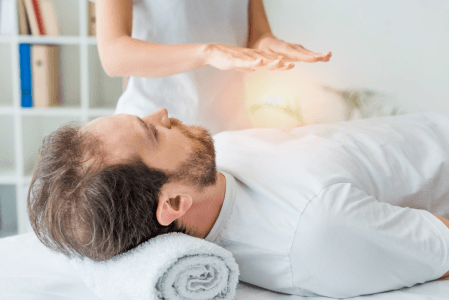 A man is laying on a bed getting a healing session from a woman.