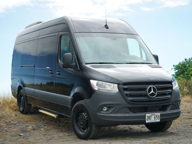 A black mercedes sprinter van is parked in a dirt field.