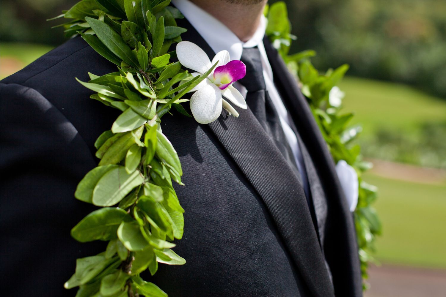A man in a suit and tie is wearing a lei around his neck.
