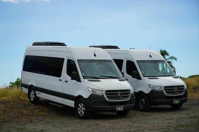 Two white vans are parked next to each other on a dirt road.