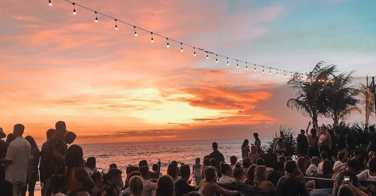 A crowd of people are gathered on the beach at sunset.