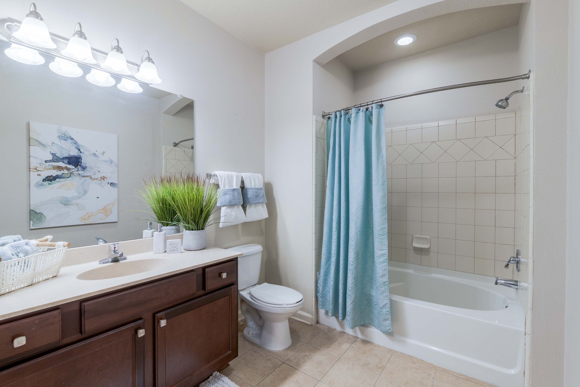 Bathroom with a brown vanity, white toilet, and a bathtub with a blue shower curtain at Grand Oaks at Ogeechee River in Savannah, GA.