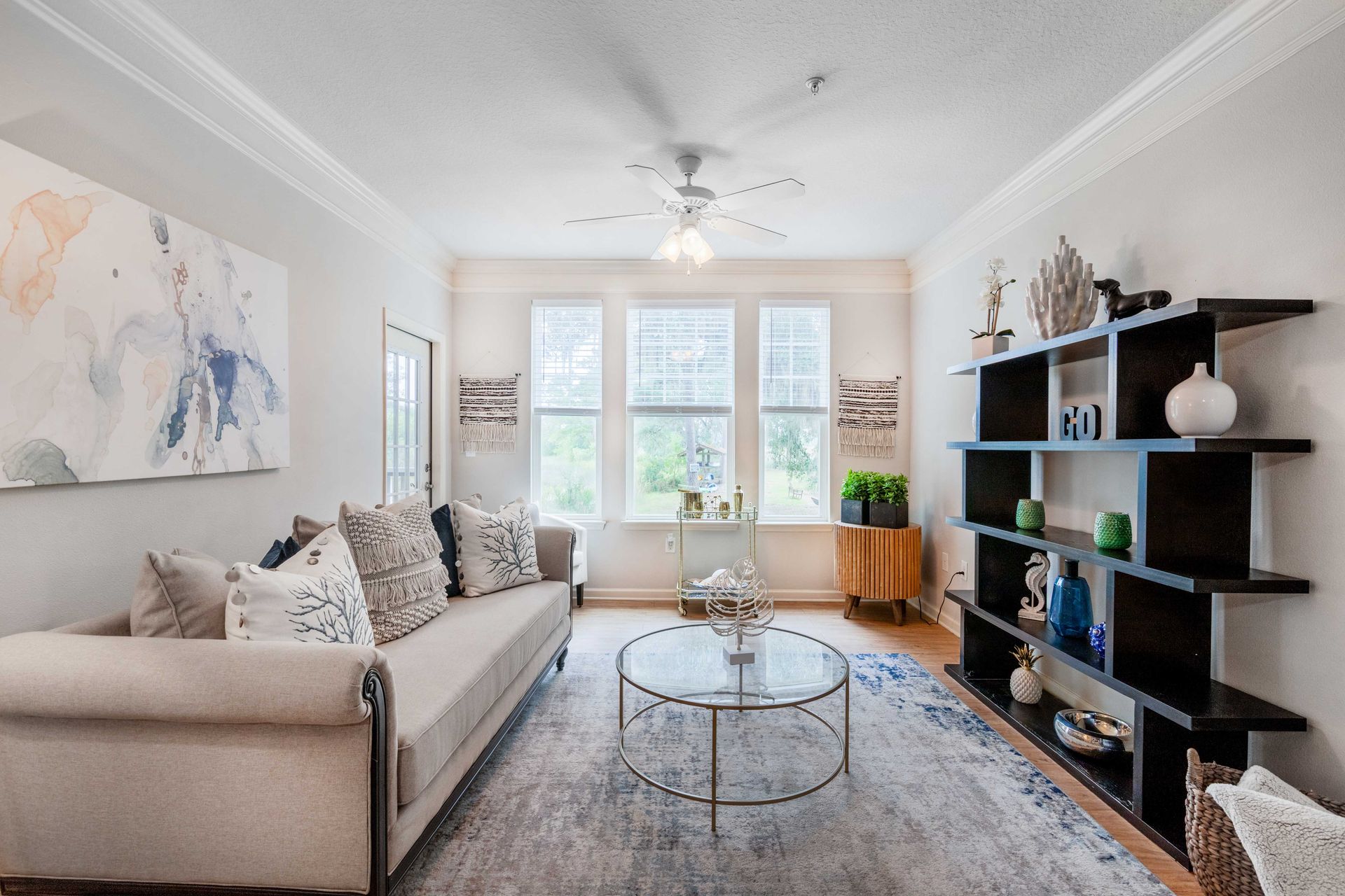 Living room with sofa, coffee table, shelves, window, artwork, and a rug at Grand Oaks at Ogeechee River in Savannah, GA.