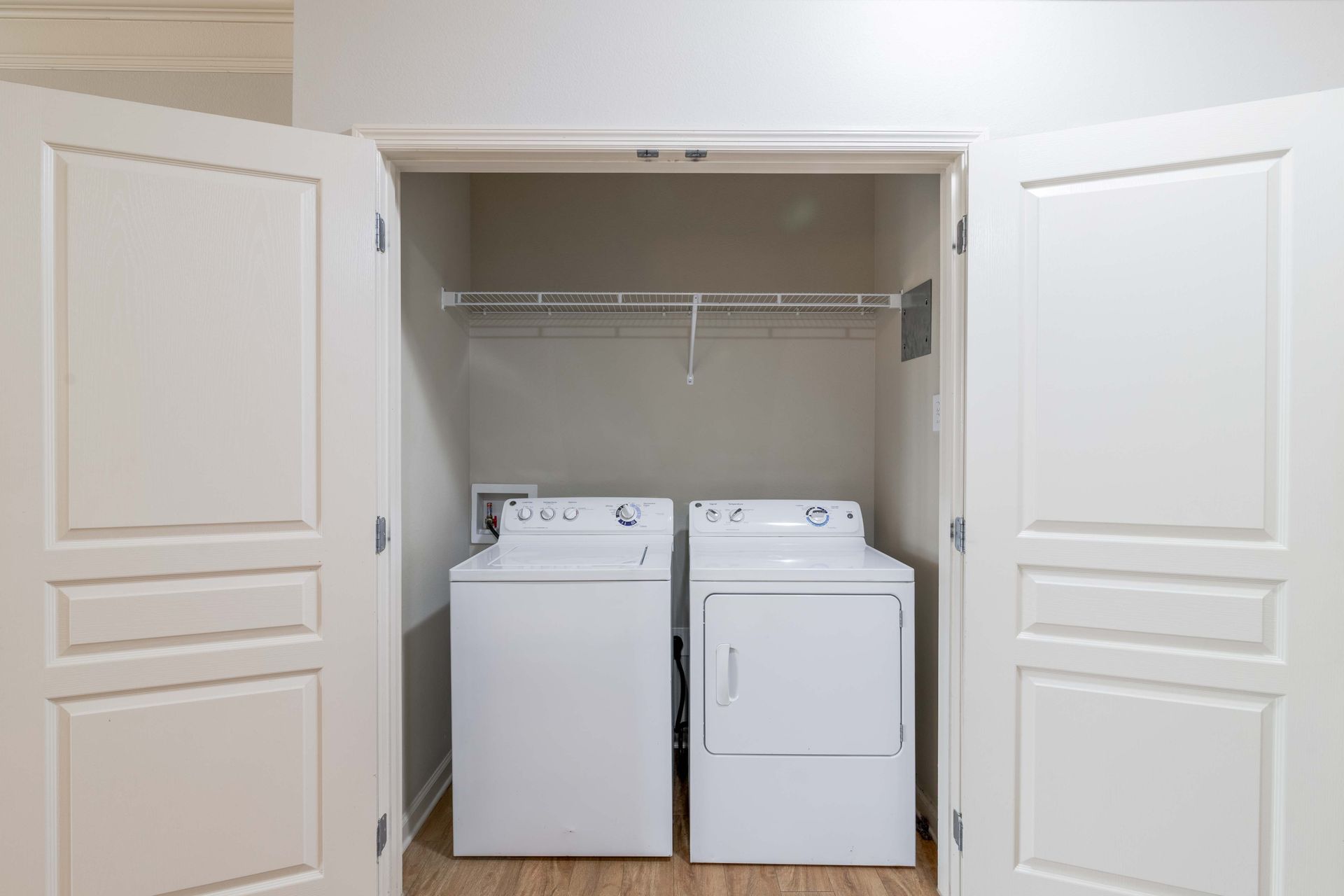White washer and dryer in a closet with open white doors; a wire rack is above at Grand Oaks at Ogeechee River in Savannah, GA.