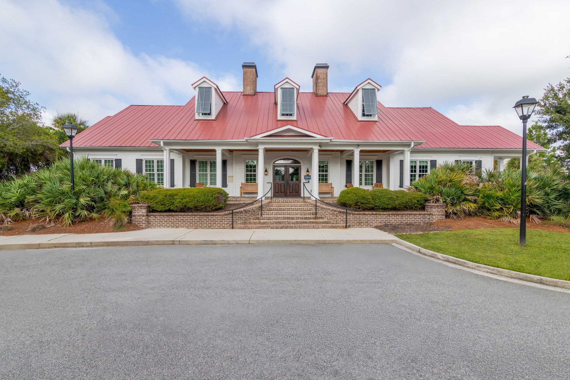 White building with red roof, porch, and dormers; driveway and landscaping in front at Grand Oaks at Ogeechee River in Savannah, GA.