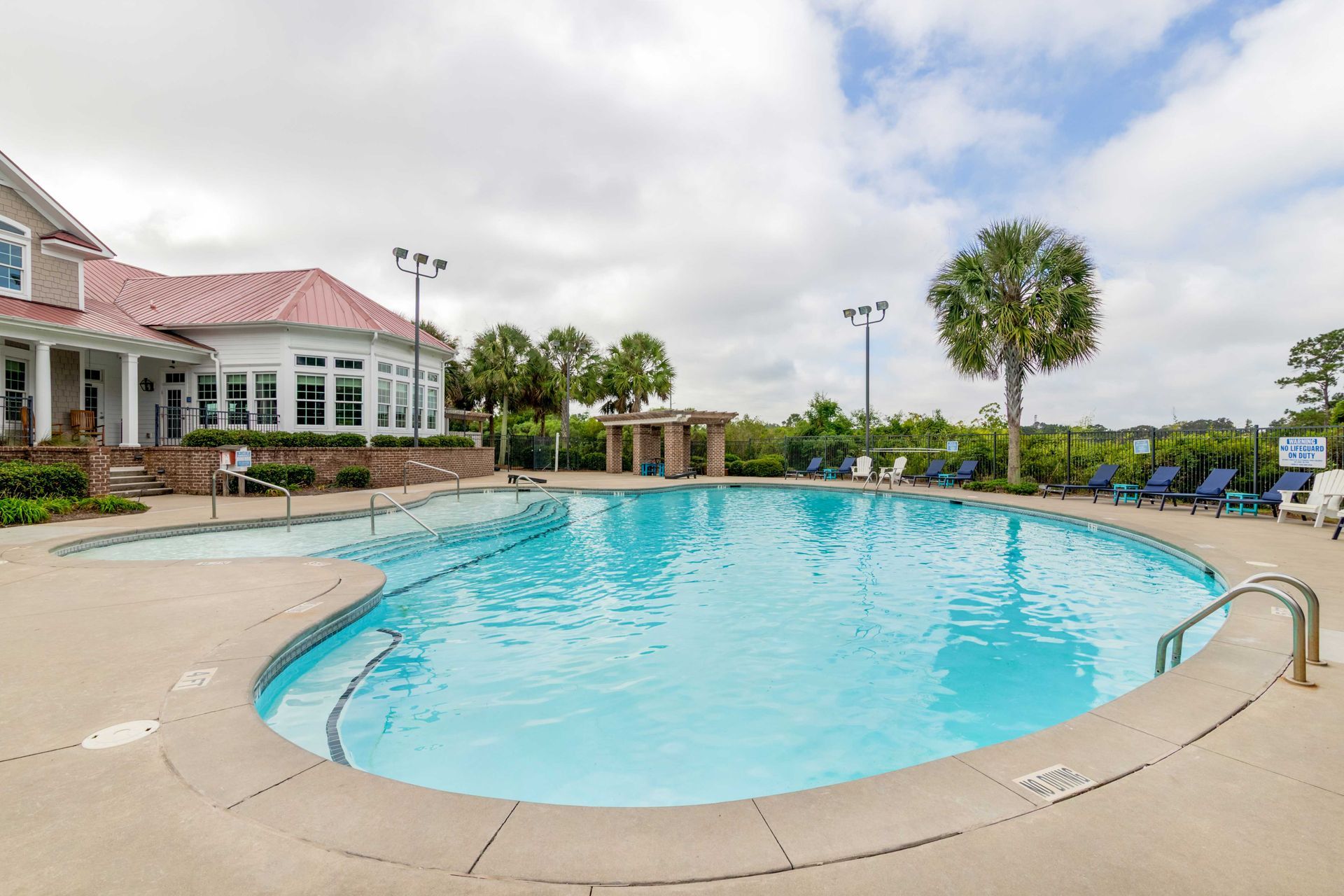 Swimming pool next to a building on a cloudy day. Palm trees and lounge chairs are present at Grand Oaks at Ogeechee River, offers pet-friendly apartments for rent in Savannah, GA.