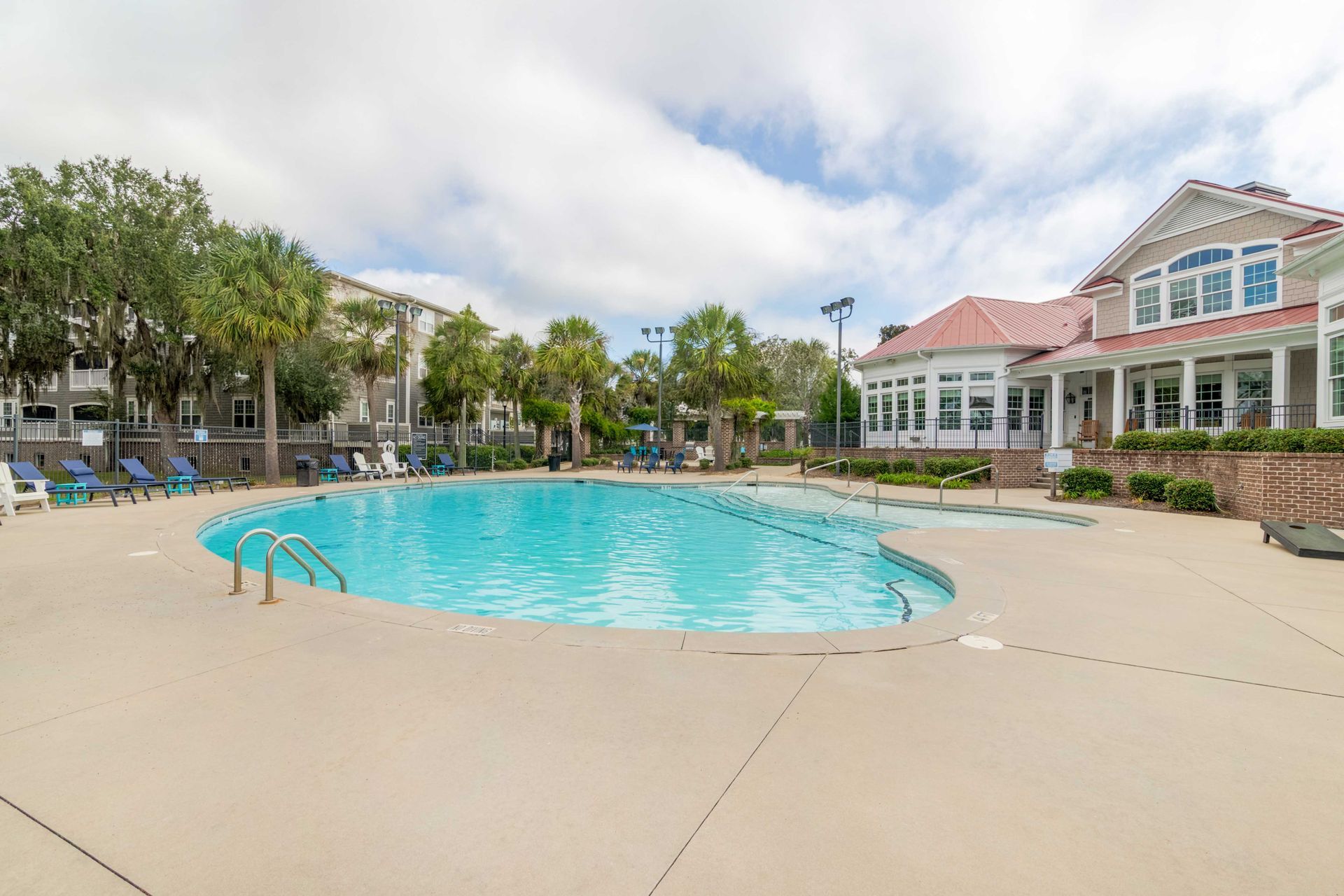 Swimming pool with lounge chairs, trees, and a building under a cloudy sky at Grand Oaks at Ogeechee River in Savannah, GA.