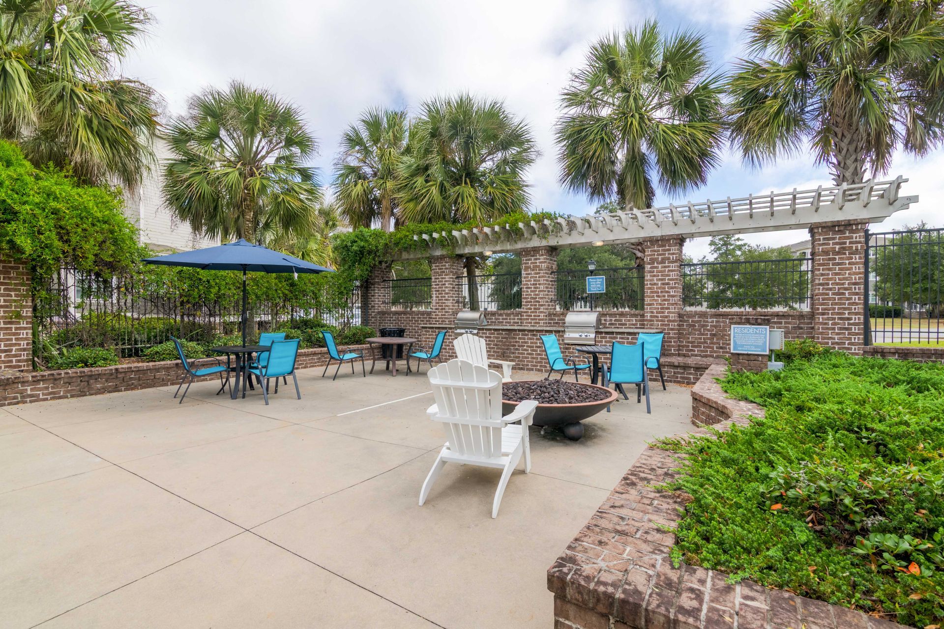 Outdoor patio with blue chairs, fire pit, grill, and pergola under palm trees at Grand Oaks at Ogeechee River in Savannah, GA.