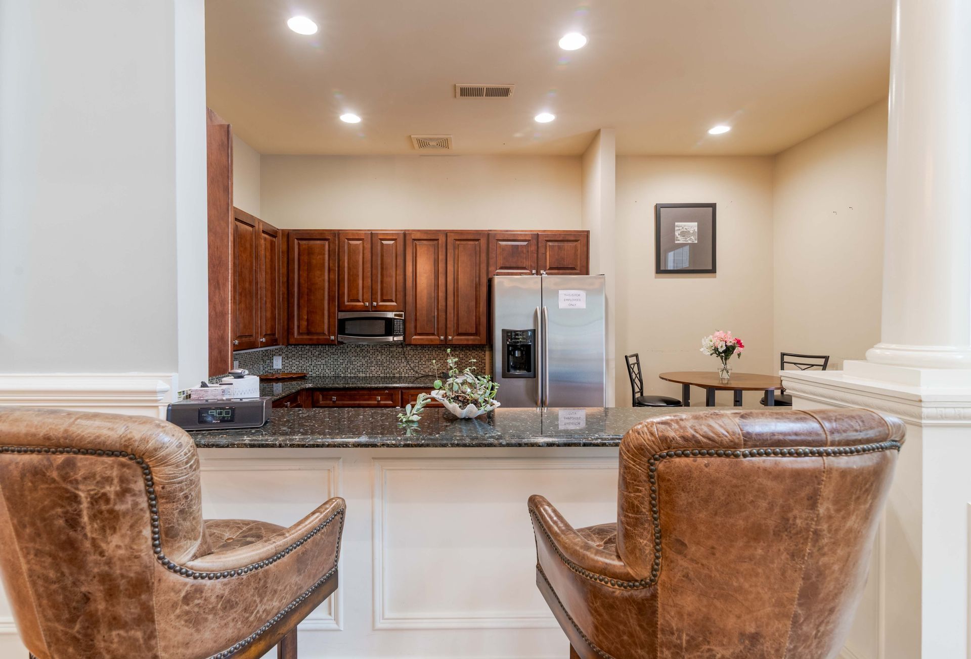 Two leather chairs face a kitchen with wood cabinets, stainless steel appliances, and a table with flowers at Grand Oaks at Ogeechee River in Savannah, GA.