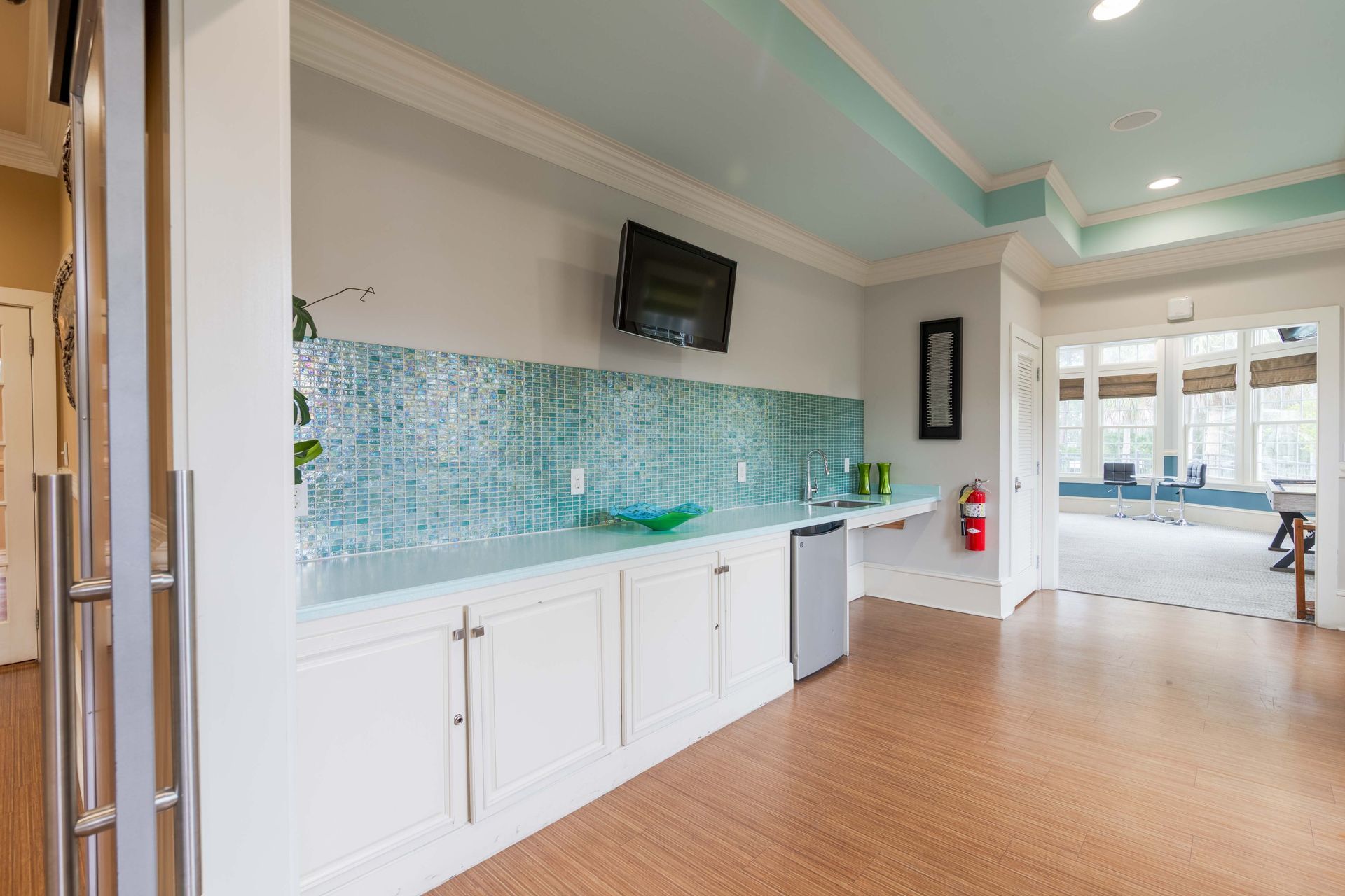 Kitchenette with a blue tile backsplash, small fridge, and a TV mounted on the wall at Grand Oaks at Ogeechee River in Savannah, GA.
