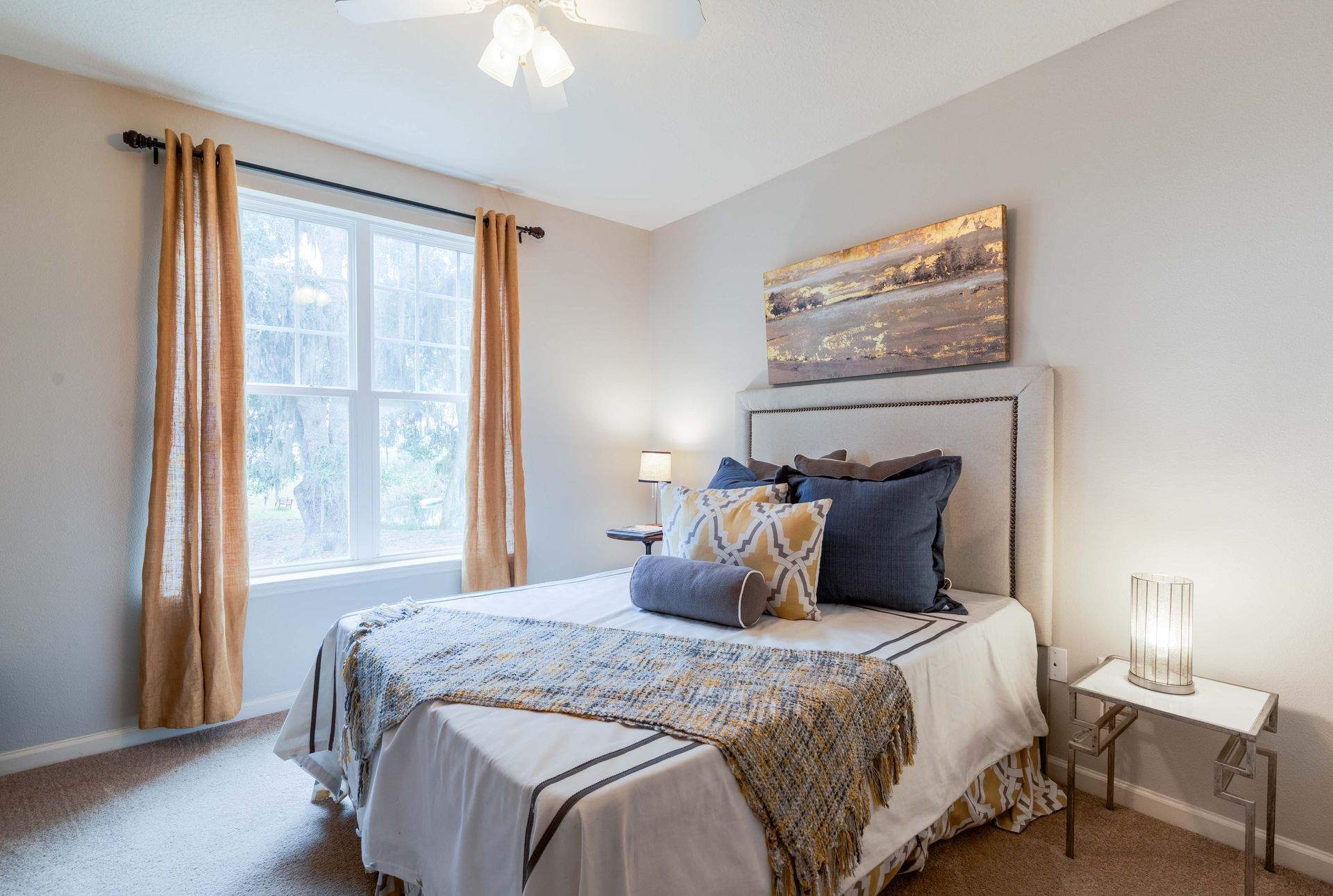 Bedroom with a bed, window, nightstands, and artwork in neutral tones at Grand Oaks at Ogeechee River in Savannah, GA.