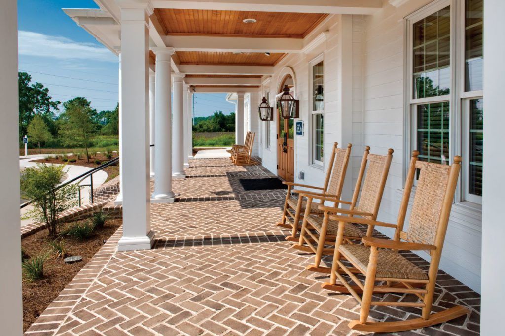 A porch with rocking chairs in front of a white building at Grand Oaks at Ogeechee River in Savannah, GA.