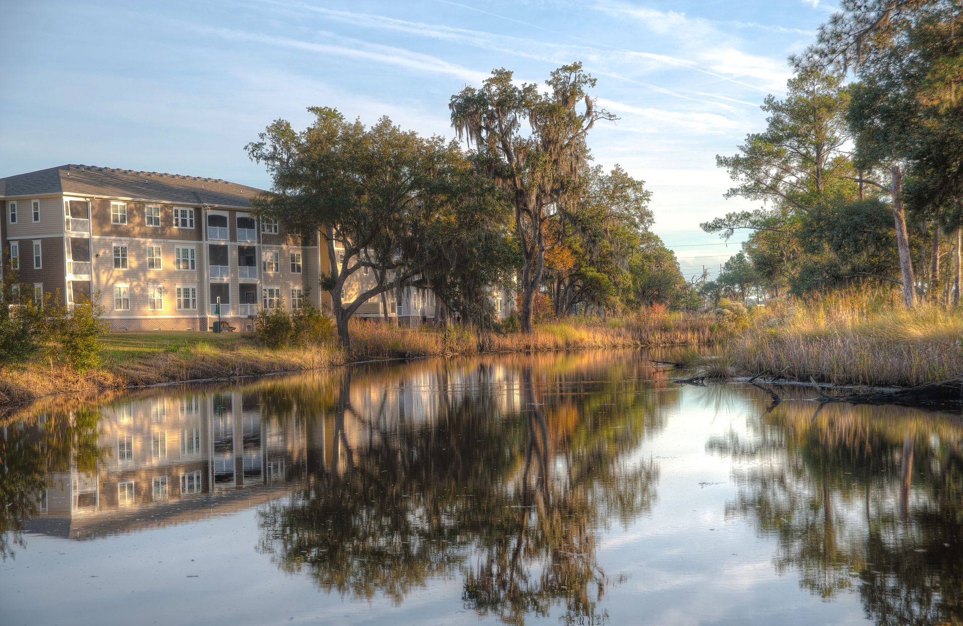 A calm canal reflects trees and a building under a partly cloudy sky at Grand Oaks at Ogeechee River in GA